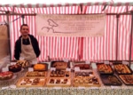 Red-striped market stall with rows of baked goods, server inside.